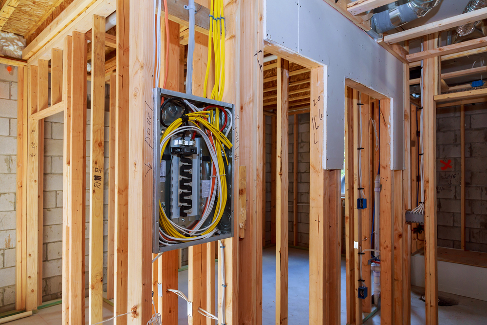 Exposed electrical panel with wiring installed on wooden framing inside a building under construction.